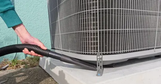 Home owner vacuums around heat pump to ensure peak efficiency
