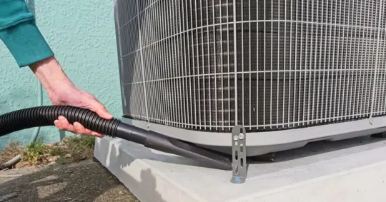 Home owner vacuums around heat pump to ensure peak efficiency