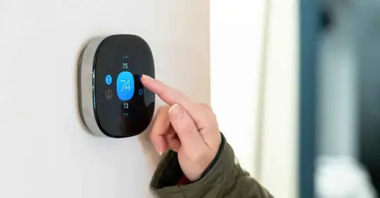 Woman adjusting temperature on digital thermostat